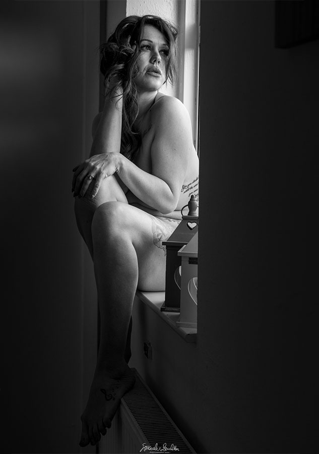 Low-key seated portrait in a dark bodysuit beside a window