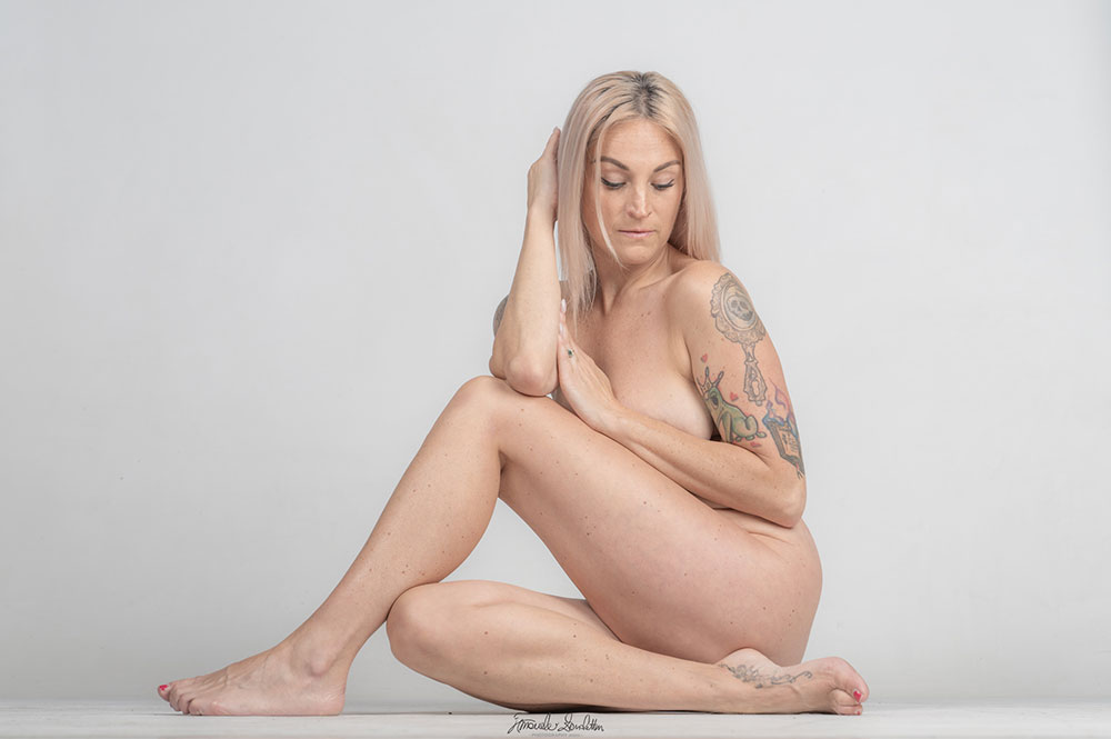 High-key nude figure seated cross-legged on a pale background