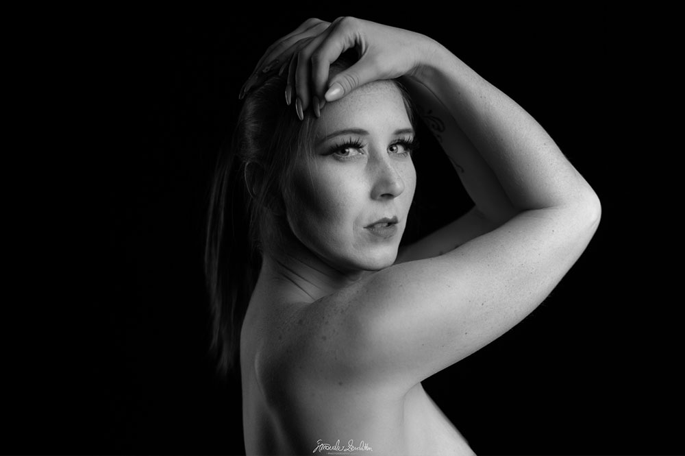 Black-and-white bare-shouldered close portrait with one arm raised