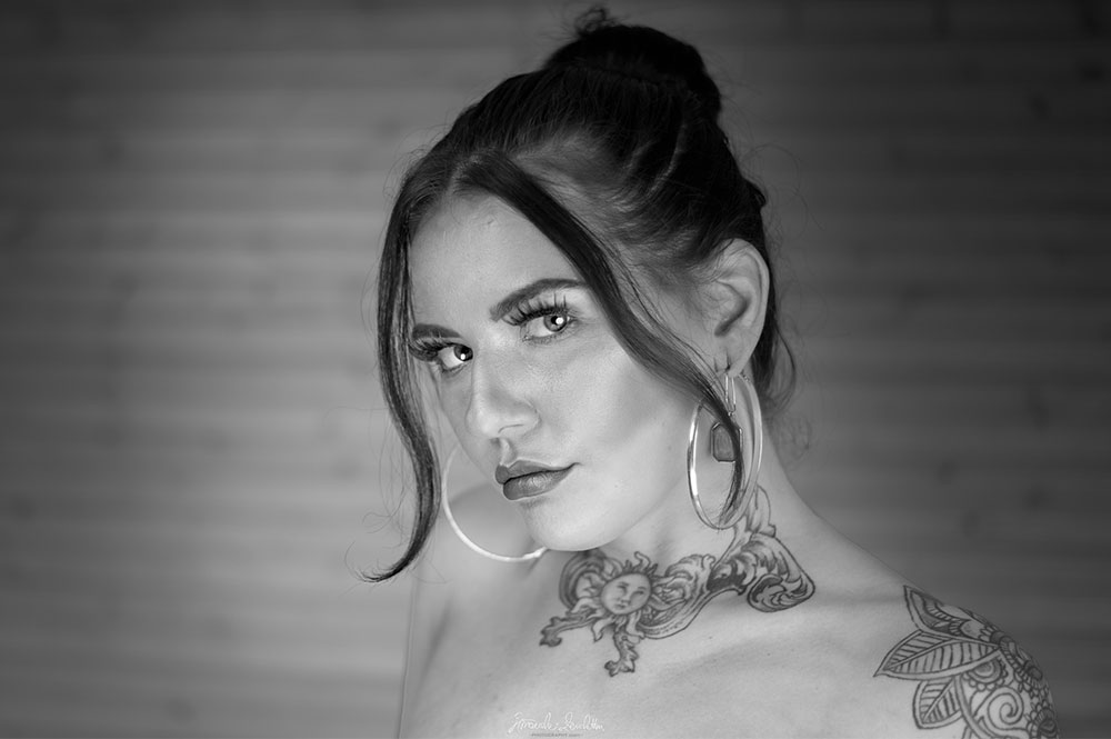 Black-and-white bare-shouldered close portrait with neck tattoo